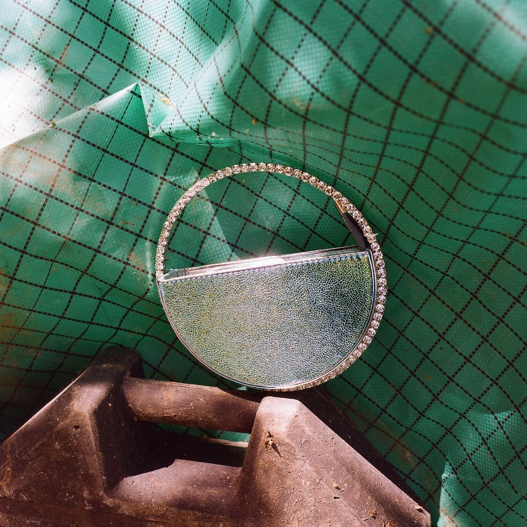 Circular purse with rhinestones rests on a dark gray and green background in a studio shot, high-angle perspective. 