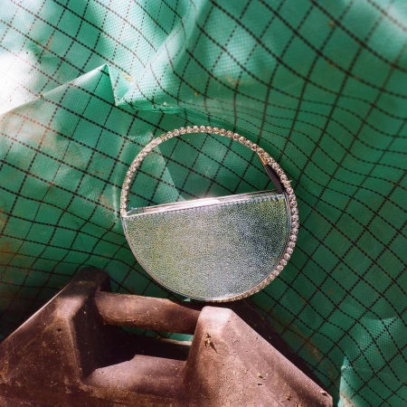 Circular purse with rhinestones rests on a dark gray and green background in a studio shot, high-angle perspective. 