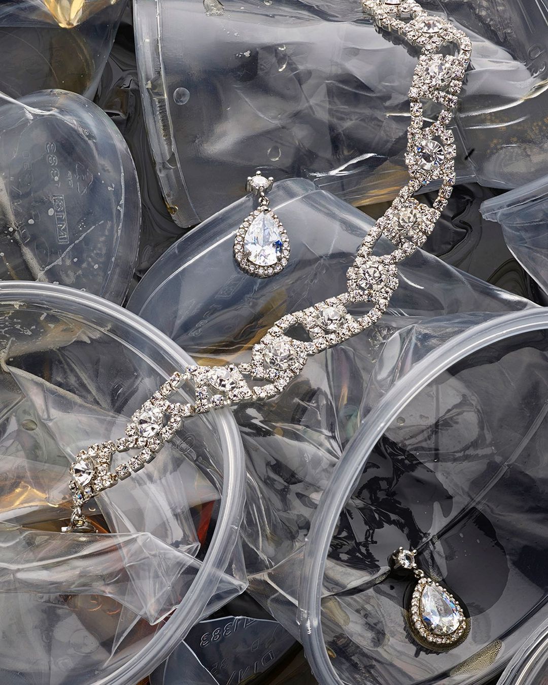 Elegant silver bracelet and drop earrings with clear stones set on a backdrop of clear plastic bags, a juxtaposition of glamour and waste.