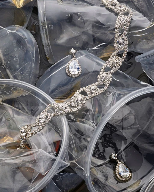 Elegant silver bracelet and drop earrings with clear stones set on a backdrop of clear plastic bags, a juxtaposition of glamour and waste.