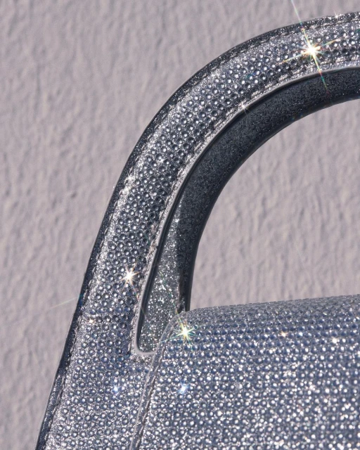 Close-up of a handle and side of a shiny silver handbag or purse covered in reflective glitter material. Fashion accessory.