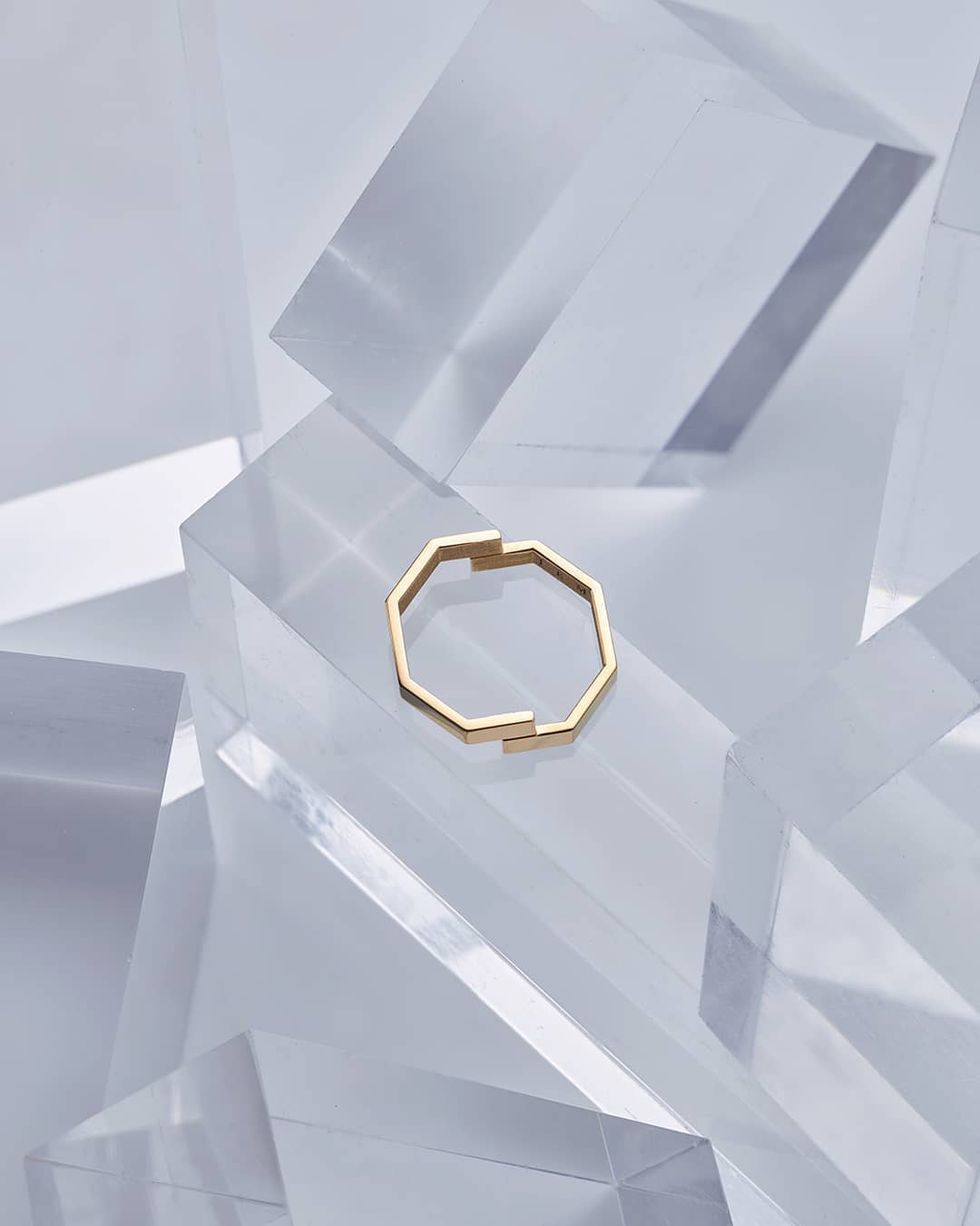 High-angle shot showcases an octagonal gold ring atop clear acrylic blocks, highlighting its minimalist design and the play of light.