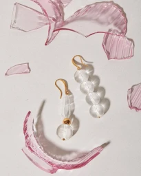 Clear glass bead earrings with gold hooks displayed on a light surface surrounded by broken translucent pink glass shards.