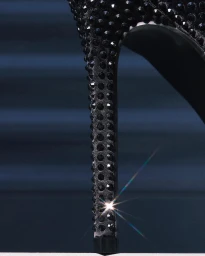Close-up macro shot of a black high heel shoe covered in rhinestones with a prominent starburst light flare on the heel.