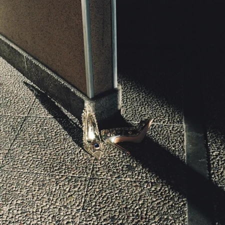 High-heeled embellished shoes resting on textured stone pavement near a concrete pillar.