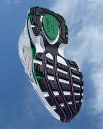 Underside of a white, green, and black Lacoste sneaker angled upward against a clear blue sky background