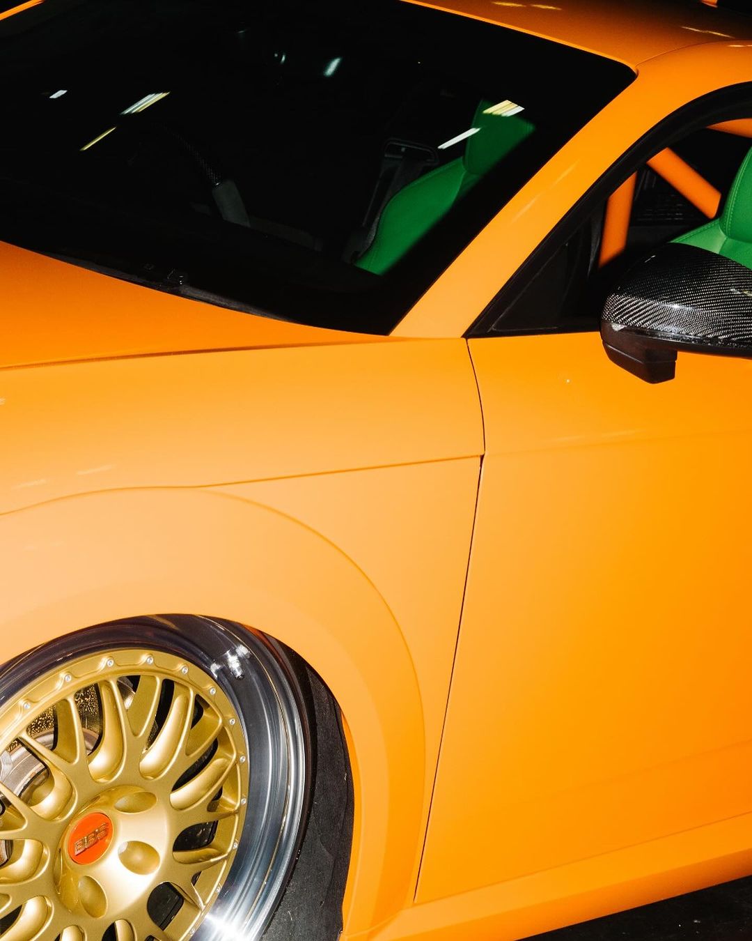 Close-up of a bright orange Audi TT featuring gold rims and carbon fiber mirror. Car enthusiasts will appreciate this custom vehicle.