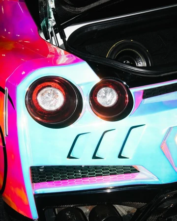 Close-up of a car's rear with the trunk open, showcasing vibrant pink and blue iridescent paint, modern taillights, and a glimpse of the interior.