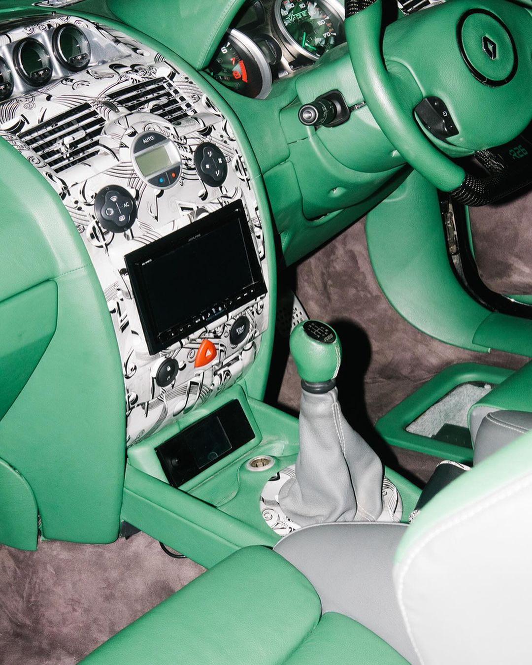 Car interior showcasing mint green leather upholstery, dashboard with music note pattern, gear shift, and steering wheel.