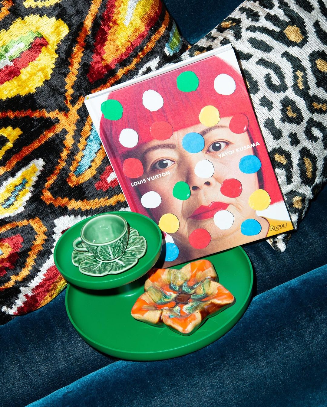 Coffee cup with saucer, a decorative plate, and a book with a portrait of Yayoi Kusama with polka dots and the Louis Vuitton logo.