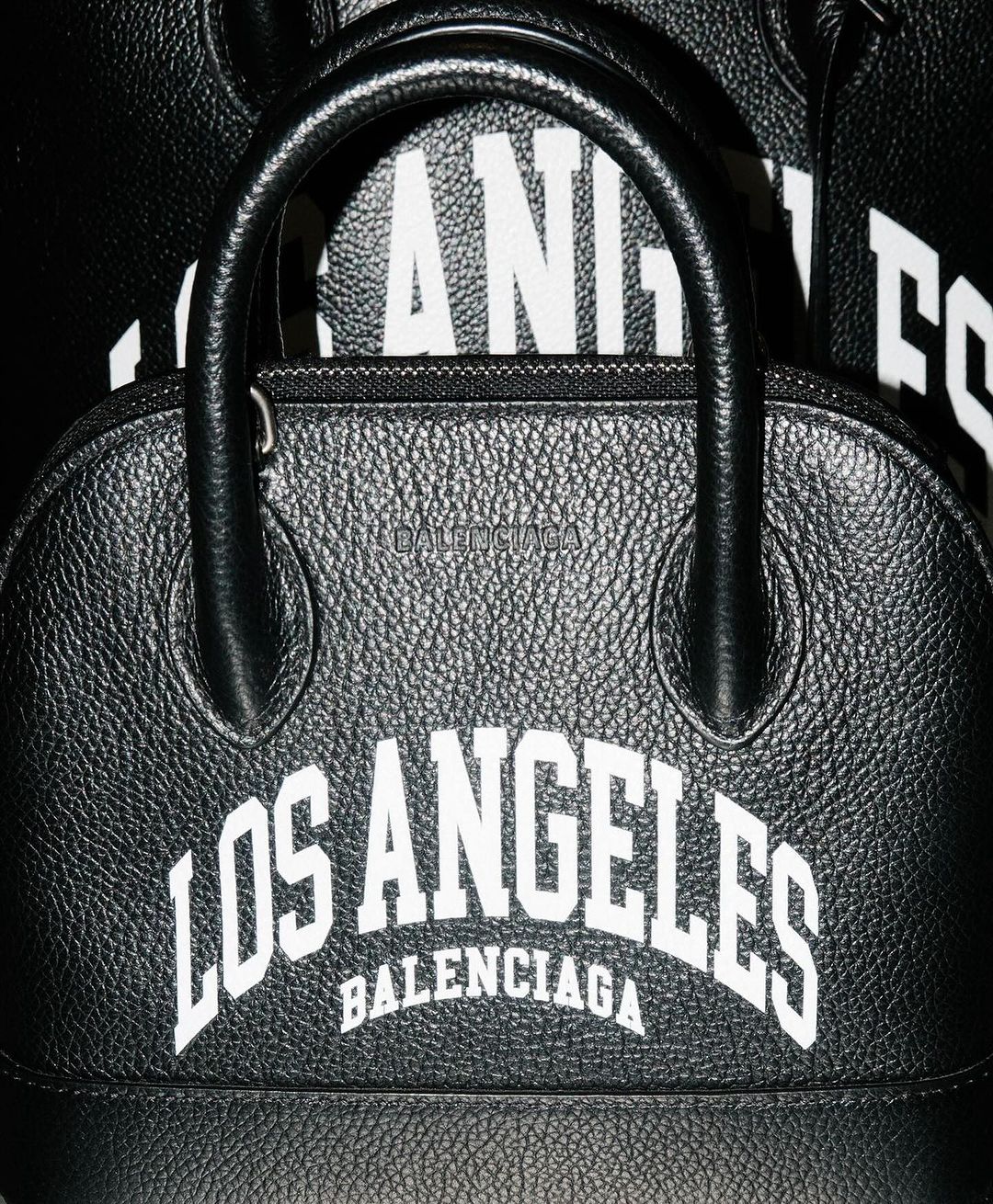 Close-up of black leather Balenciaga purse with white 'Los Angeles' text, showcasing fashion accessory and brand in studio setting.