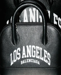 Close-up product shot of two black textured leather bags featuring prominent white Los Angeles lettering against a dark background.