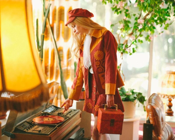 Woman in a vintage outfit plays a vinyl record on a turntable in a cozy room with warm lighting and retro decor, creating a nostalgic scene.