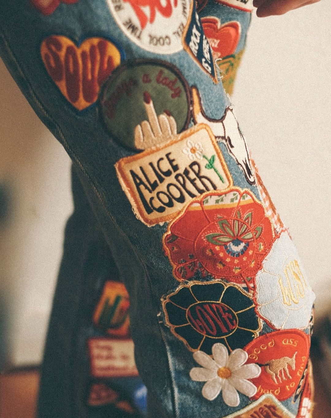 Close-up of blue denim jeans covered in various colorful embroidered patches and appliques, showing a whimsical and artistic design.