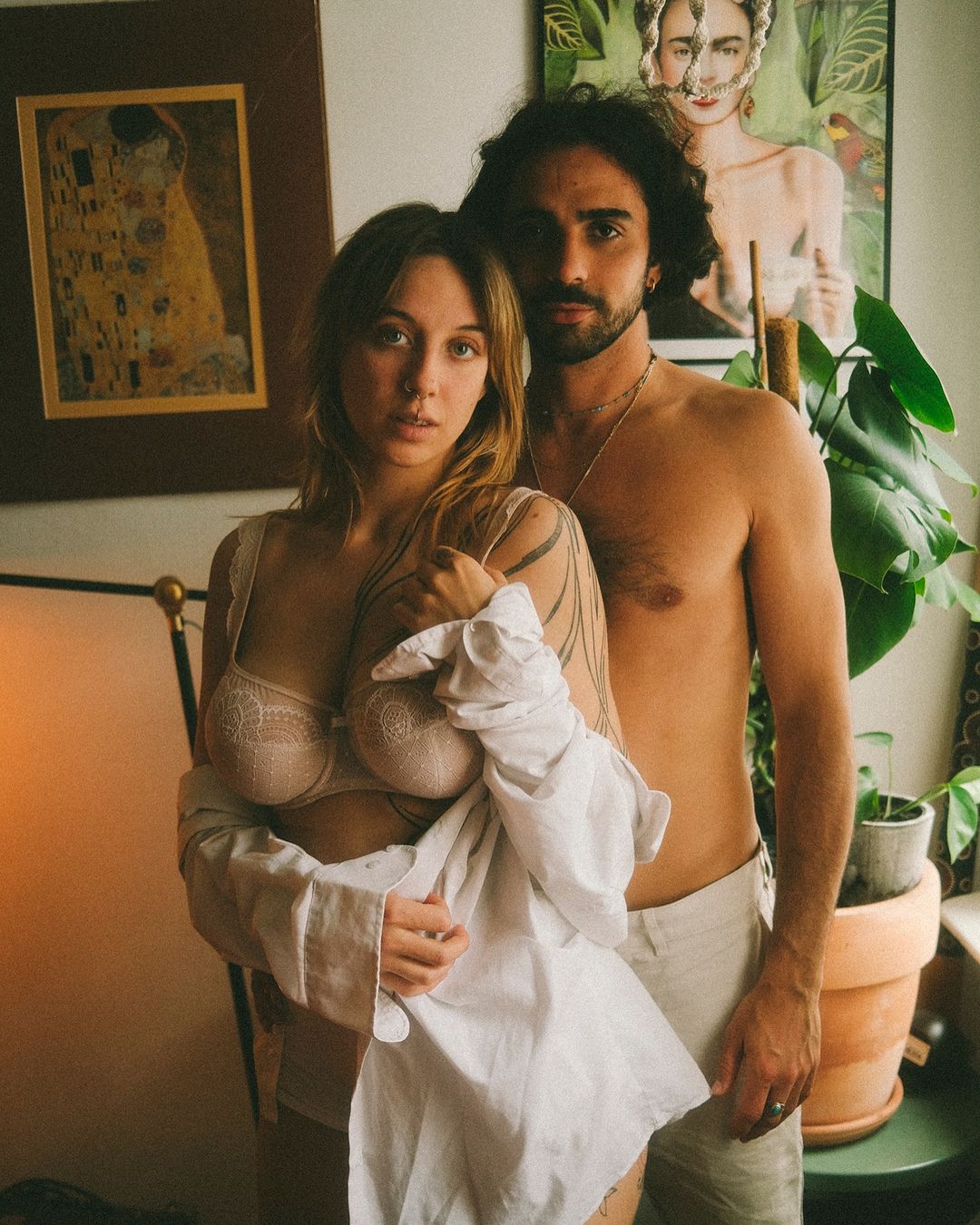 Intimate portrait of a young couple in a domestic interior, featuring a shirtless man and a woman in lingerie, with art in the background.