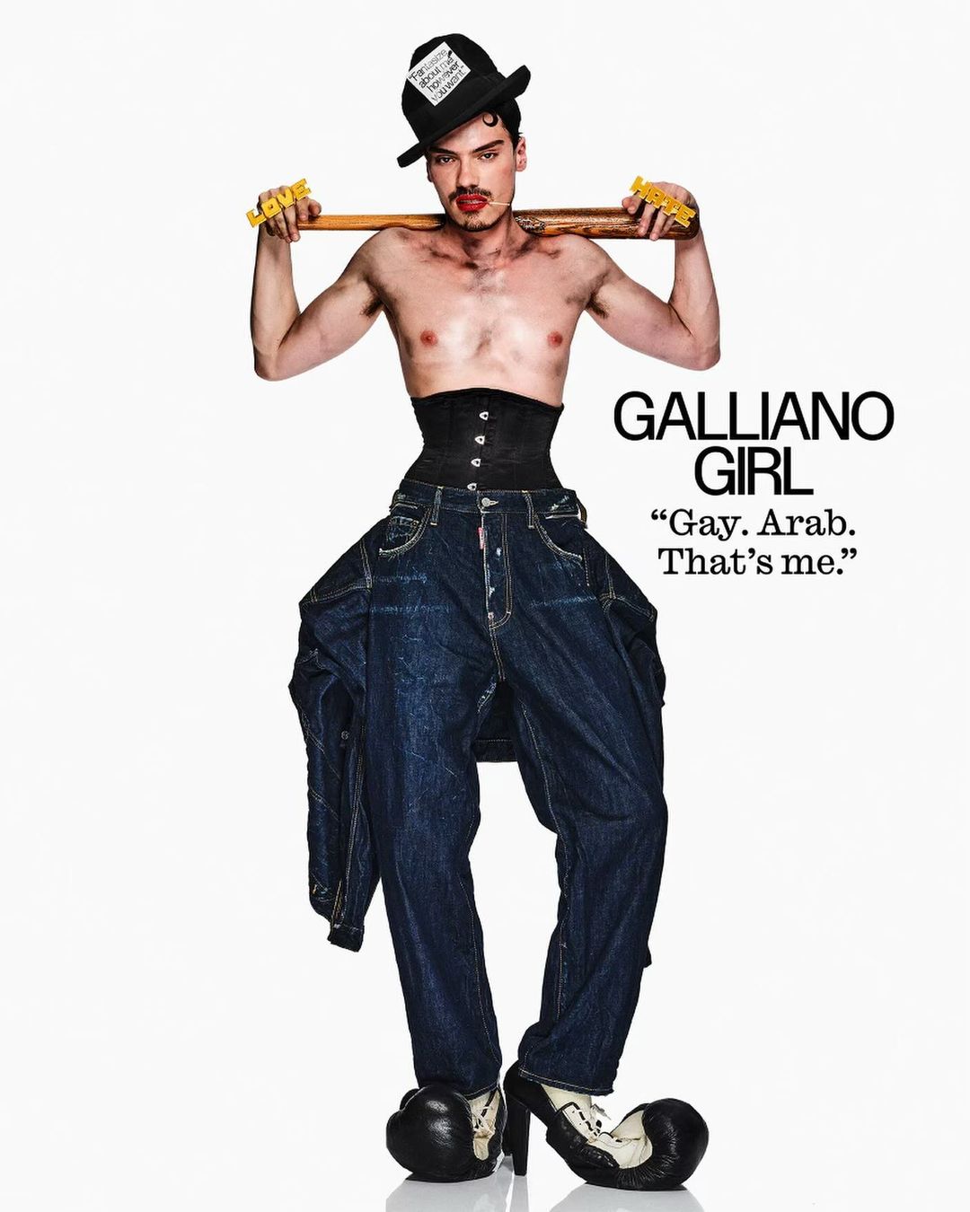 Fashion image featuring a shirtless adult male in high heels, a corset, and oversized jeans, posing with a bat on a white backdrop.