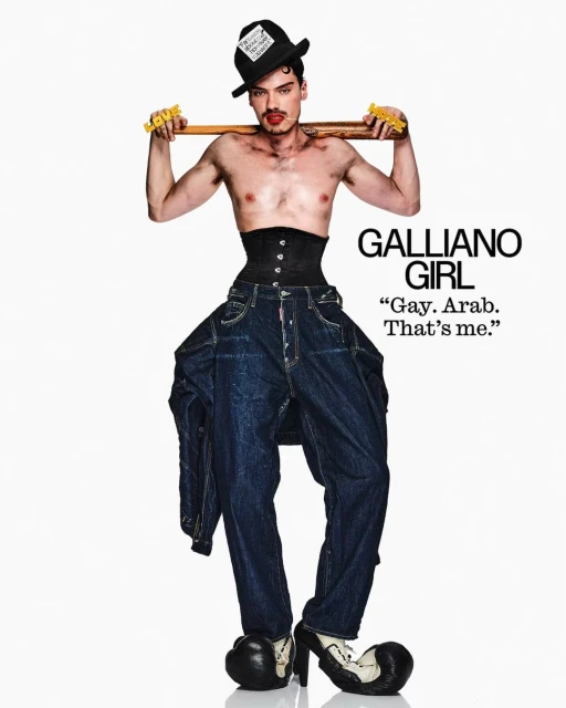 Fashion image featuring a shirtless adult male in high heels, a corset, and oversized jeans, posing with a bat on a white backdrop.