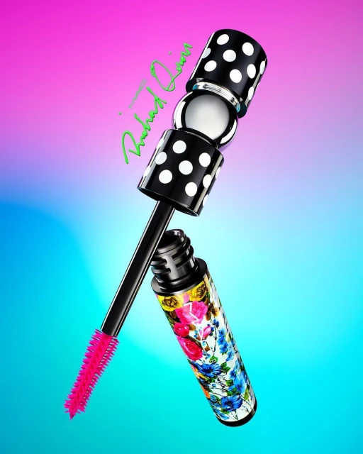 High-angle studio shot of a mascara tube with a floral pattern and a wand with a pink brush against a gradient pink and blue backdrop.