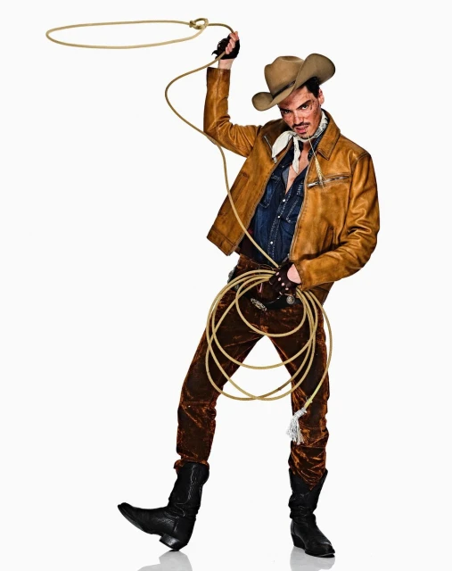 Man in cowboy attire holding a lasso in a studio shot. Wearing a hat, jacket, and boots, he embodies a Western aesthetic with a playful twist.
