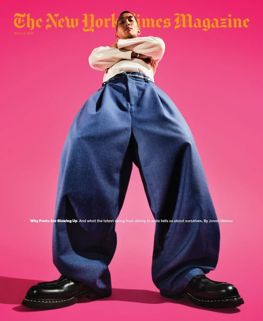New York Times Magazine cover featuring a person wearing very wide leg blue pants, a white shirt, and black shoes against pink backdrop.