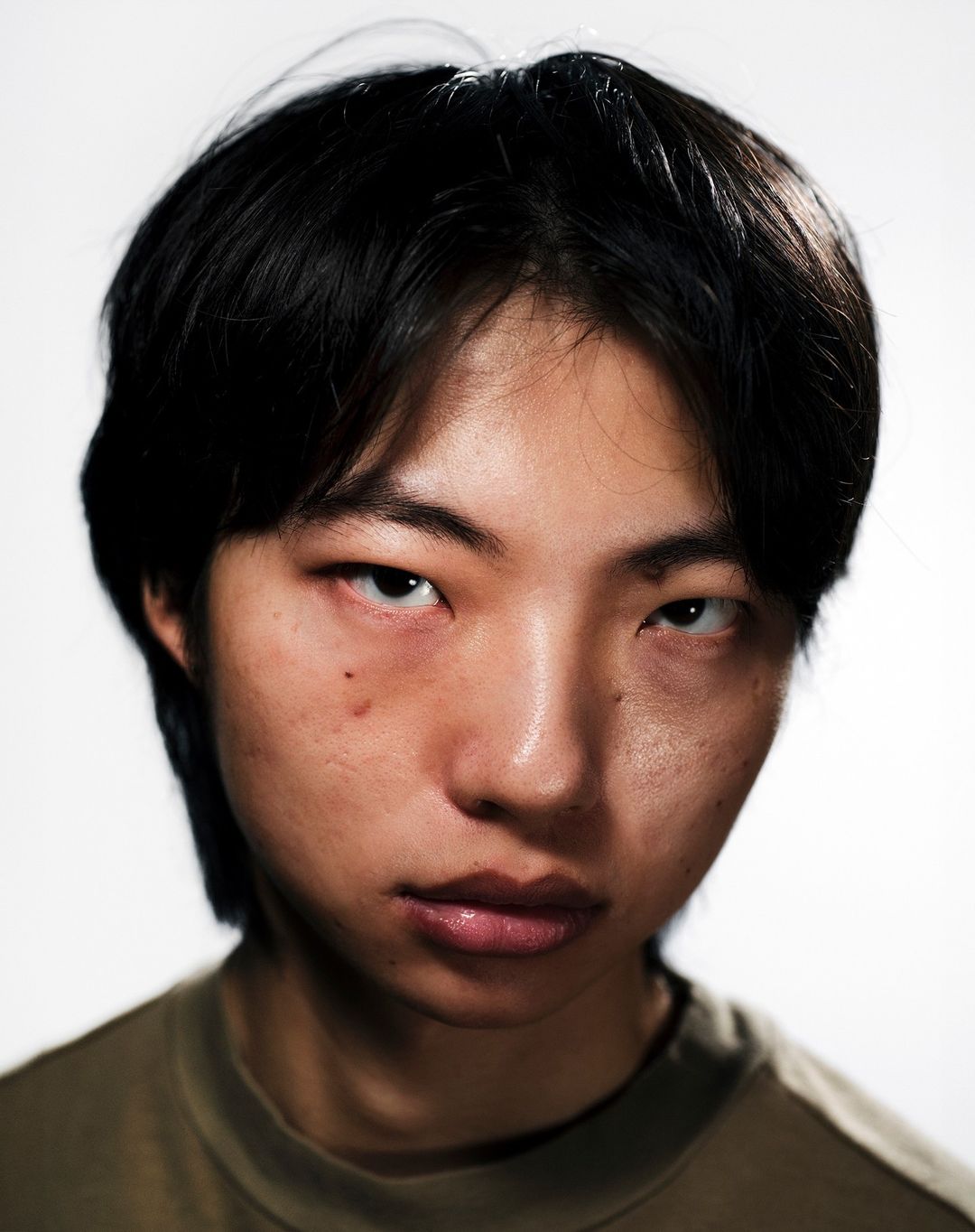 Portrait of an Asian adult male with dark hair wearing a green shirt against a white background, captured in a close-up shot.