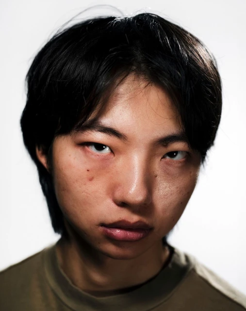 Portrait of an Asian adult male with dark hair wearing a green shirt against a white background, captured in a close-up shot.
