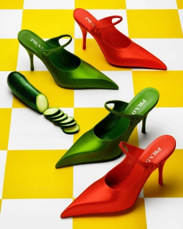 Still life of two pairs of women's heeled shoes, one green and one red, placed among zucchini on a yellow and white checkered surface.