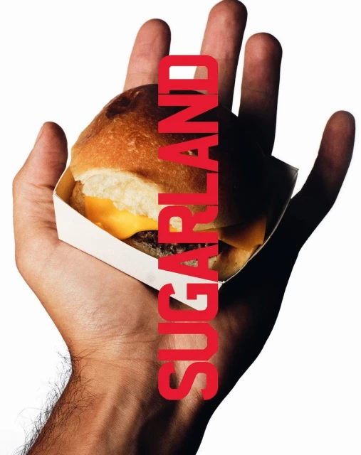 Close-up of a cheeseburger in a white cardboard container being held in a human hand, with red capitalized text overlay.