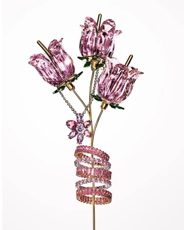 Crystal sculpture featuring three pink flower blossoms, a flower pendant, and pink gemstone rings wound around a golden stem, on white.