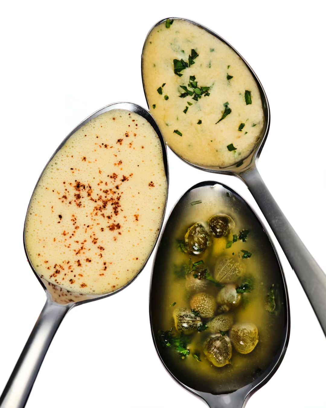 Overhead shot of three spoons filled with different sauces: a light sauce with herbs, a dark sauce with herbs, and a sauce with spices.