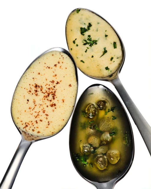 Overhead shot of three spoons filled with different sauces: a light sauce with herbs, a dark sauce with herbs, and a sauce with spices.