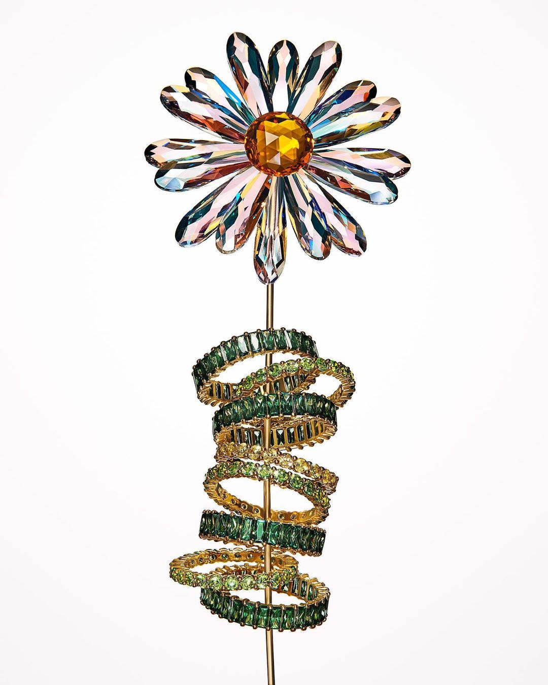 Close-up studio shot of crystal flower and green crystal rings on gold-tone stem against white background.