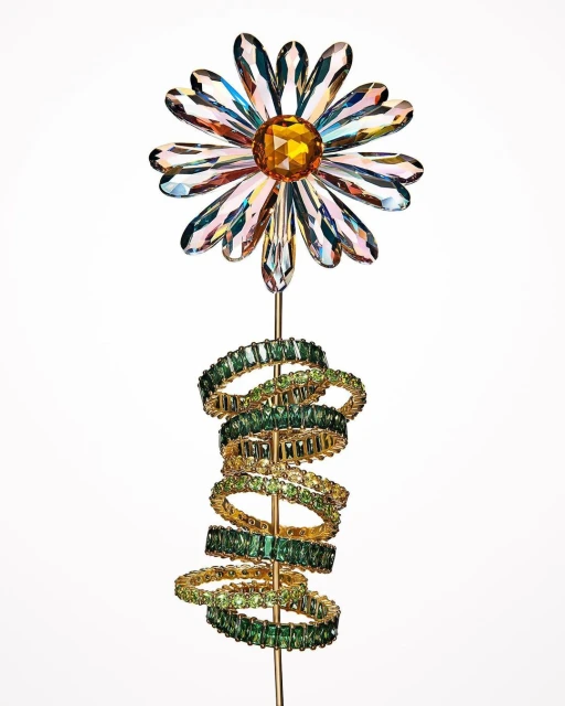 Close-up studio shot of crystal flower and green crystal rings on gold-tone stem against white background.