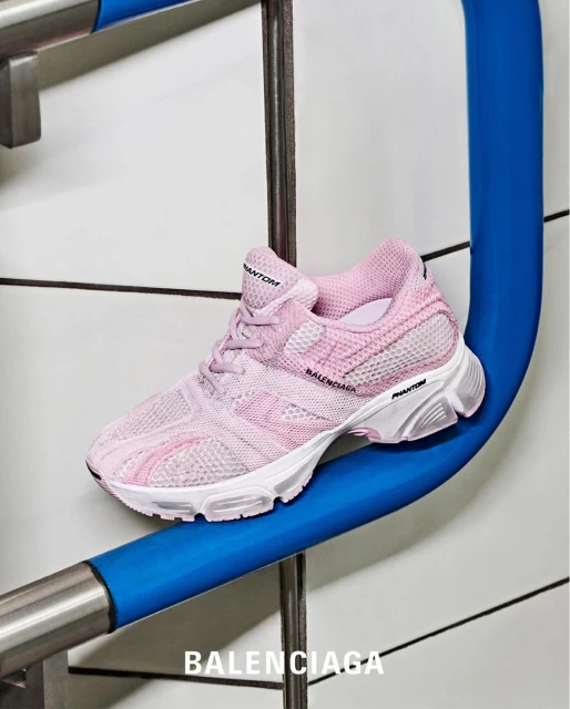Pink Balenciaga Phantom sneaker on blue steel bar against white tile wall. Close-up shot of shoe in studio lighting.