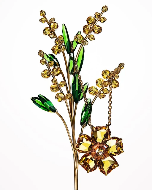 Close-up studio shot of a decorative art sculpture featuring crystal and glass elements in the shape of a flower and a blooming branch.