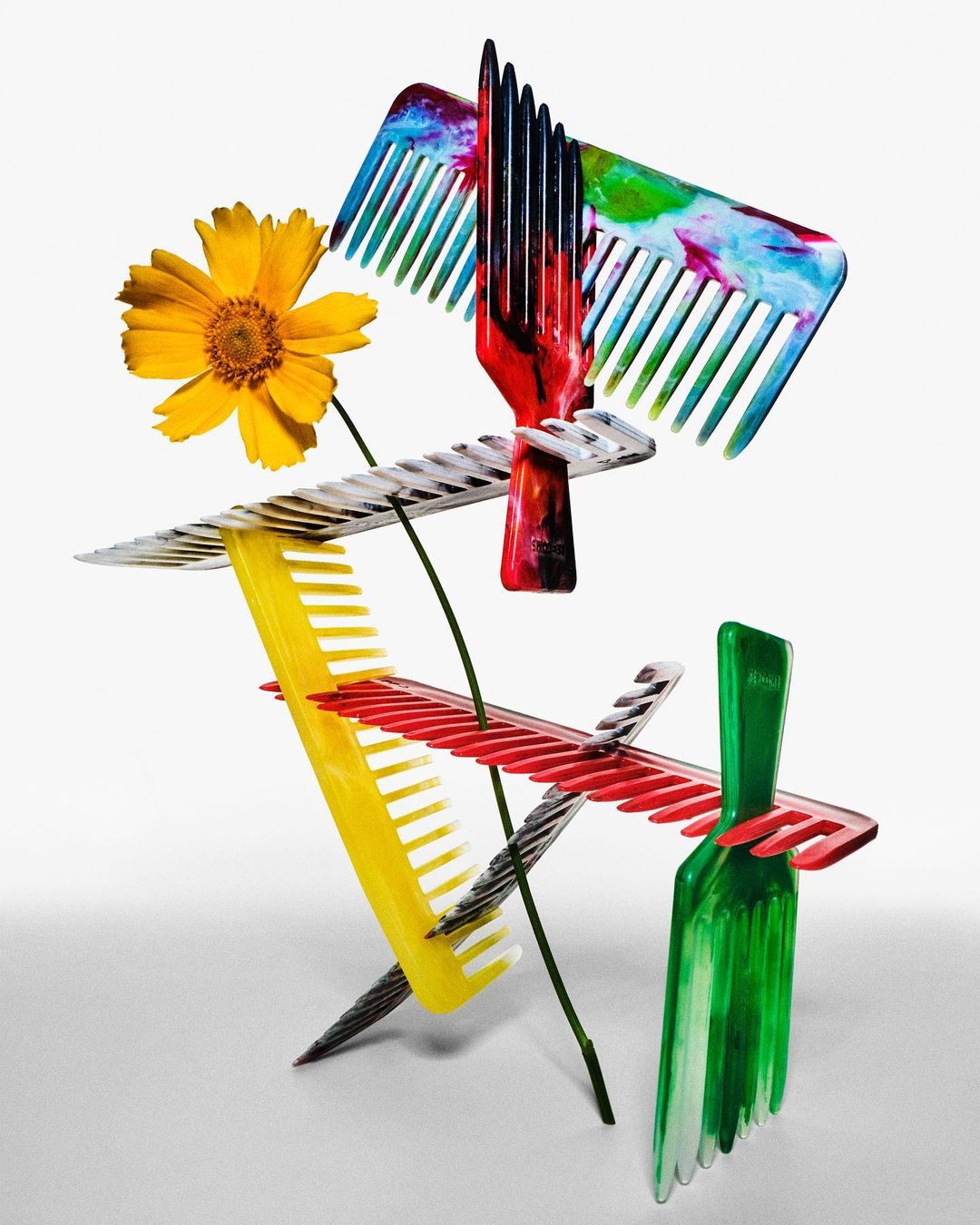 Artistic still life arrangement featuring colorful combs stacked creatively with a yellow flower against a clean white background.