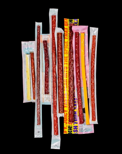 Arrangement of assorted meat sticks and cheese sticks in packaging on a black background, offering a savory snack selection.