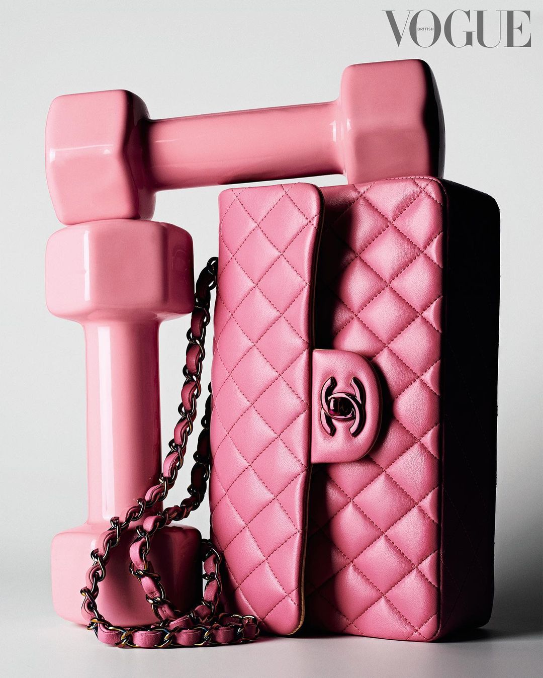 Still life studio shot of a pink Chanel handbag resting against a set of pink weights, with the Vogue logo in the corner.