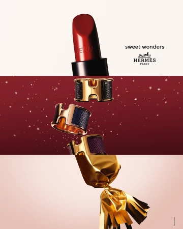 Hermès beauty product still life: lipstick, bracelets, and wrapped candy. Red, gold, and brown tones create a luxurious and festive mood.