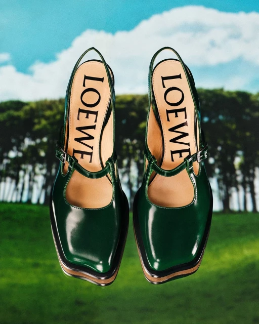 Close-up of two green Loewe shoes with the brand name visible, set against a background of trees and a blue sky.