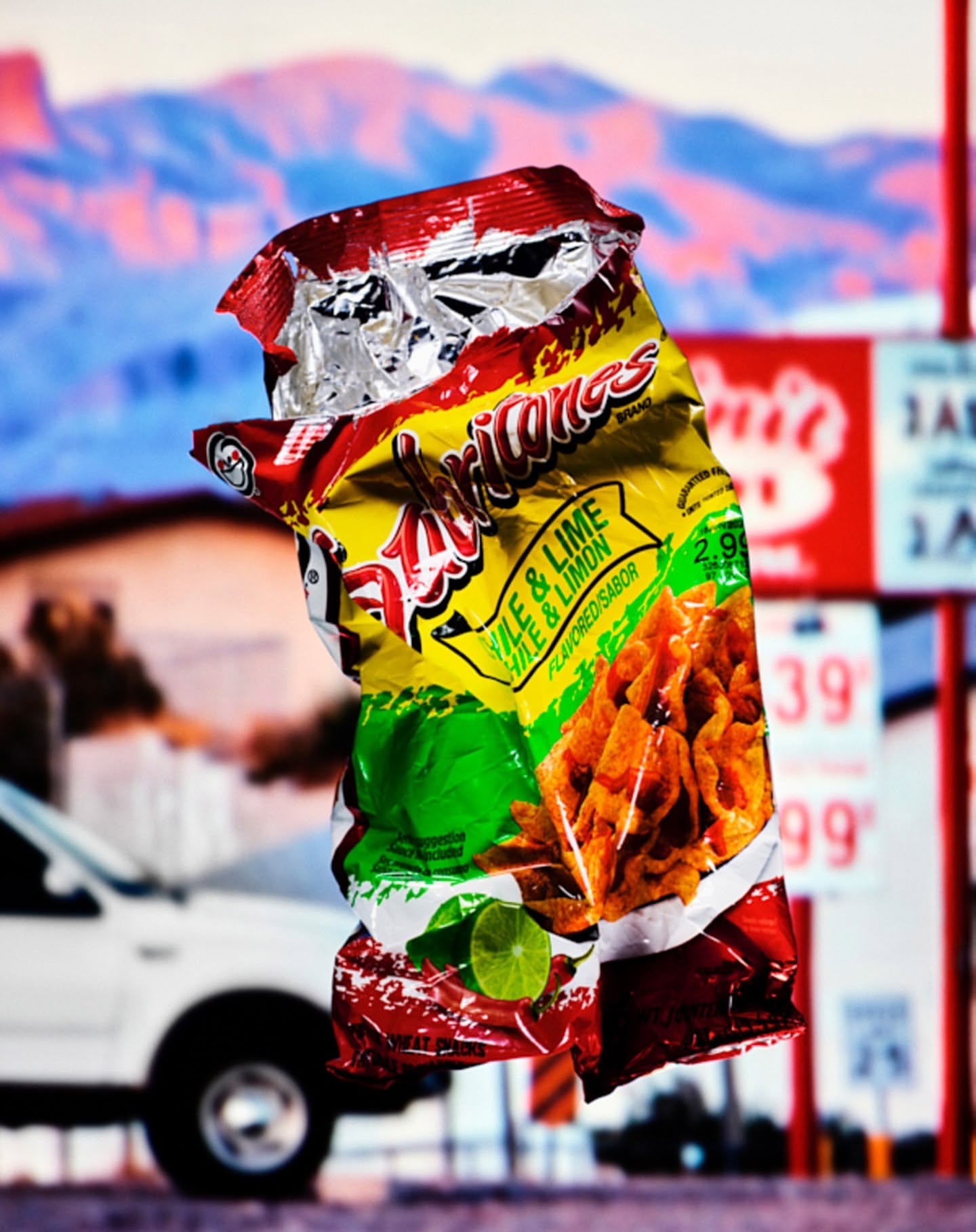 Crushed yellow snack bag with lime flavor in front of a blur of a gas station and mountain range landscape at daytime.