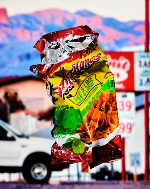 Crushed yellow snack bag with lime flavor in front of a blur of a gas station and mountain range landscape at daytime.
