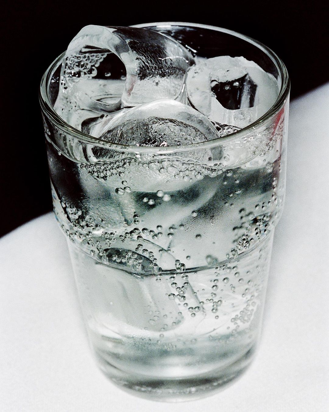 A glass of water filled with ice cubes and condensation, set against a white and dark background, evoking refreshment and coolness.