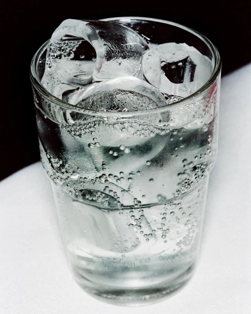 A glass of water filled with ice cubes and condensation, set against a white and dark background, evoking refreshment and coolness.