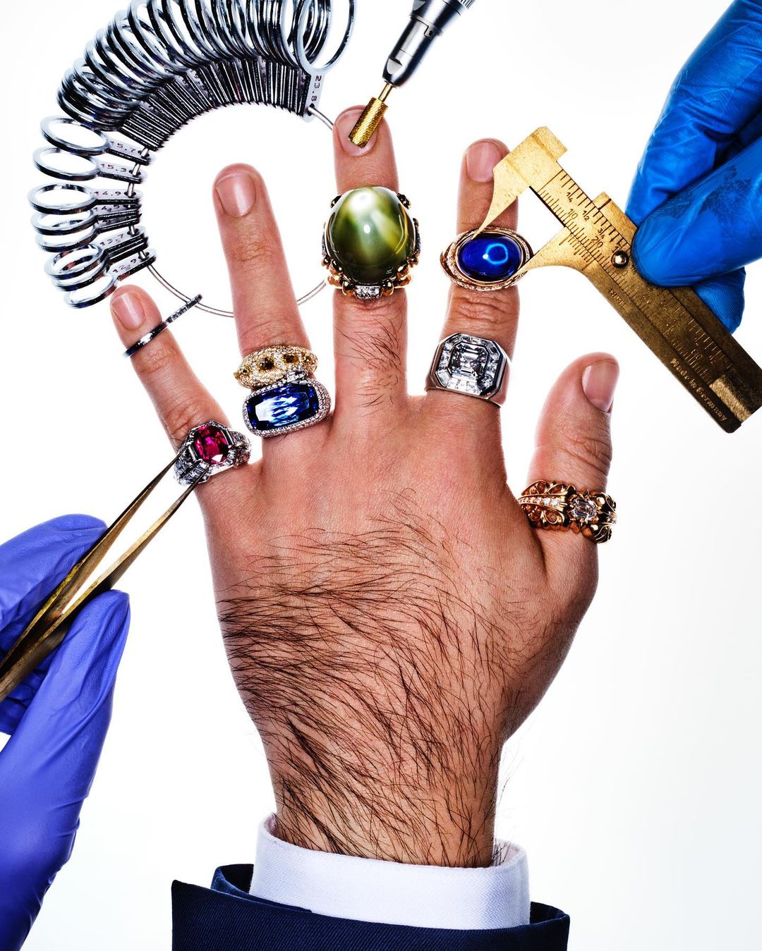 Close-up of an adult male's hand adorned with multiple jeweled rings, showcasing different gemstone colors and precious metal settings.