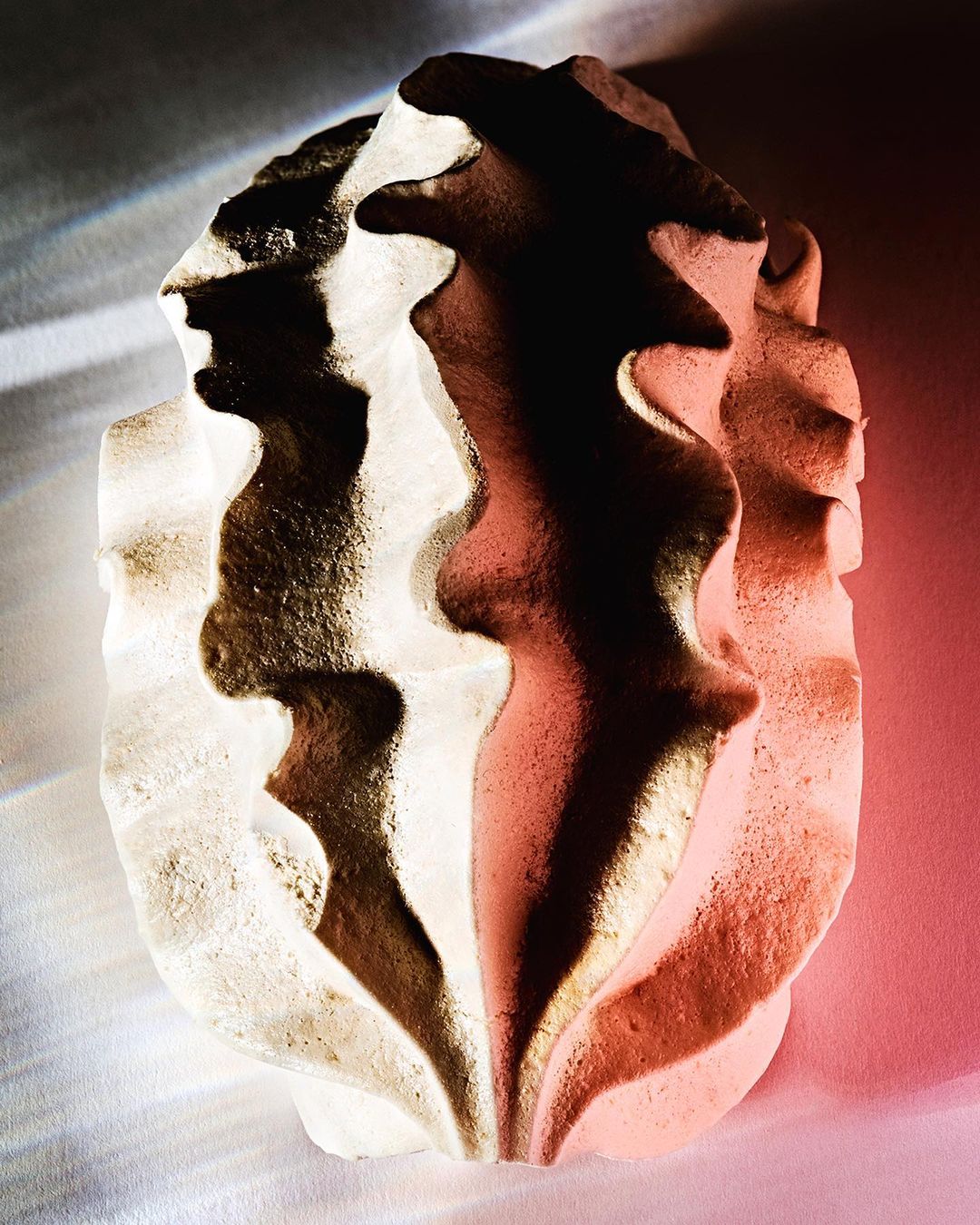 Abstract stone sculpture illuminated with dynamic lighting, showcasing rough texture and organic form in a minimalist setting.