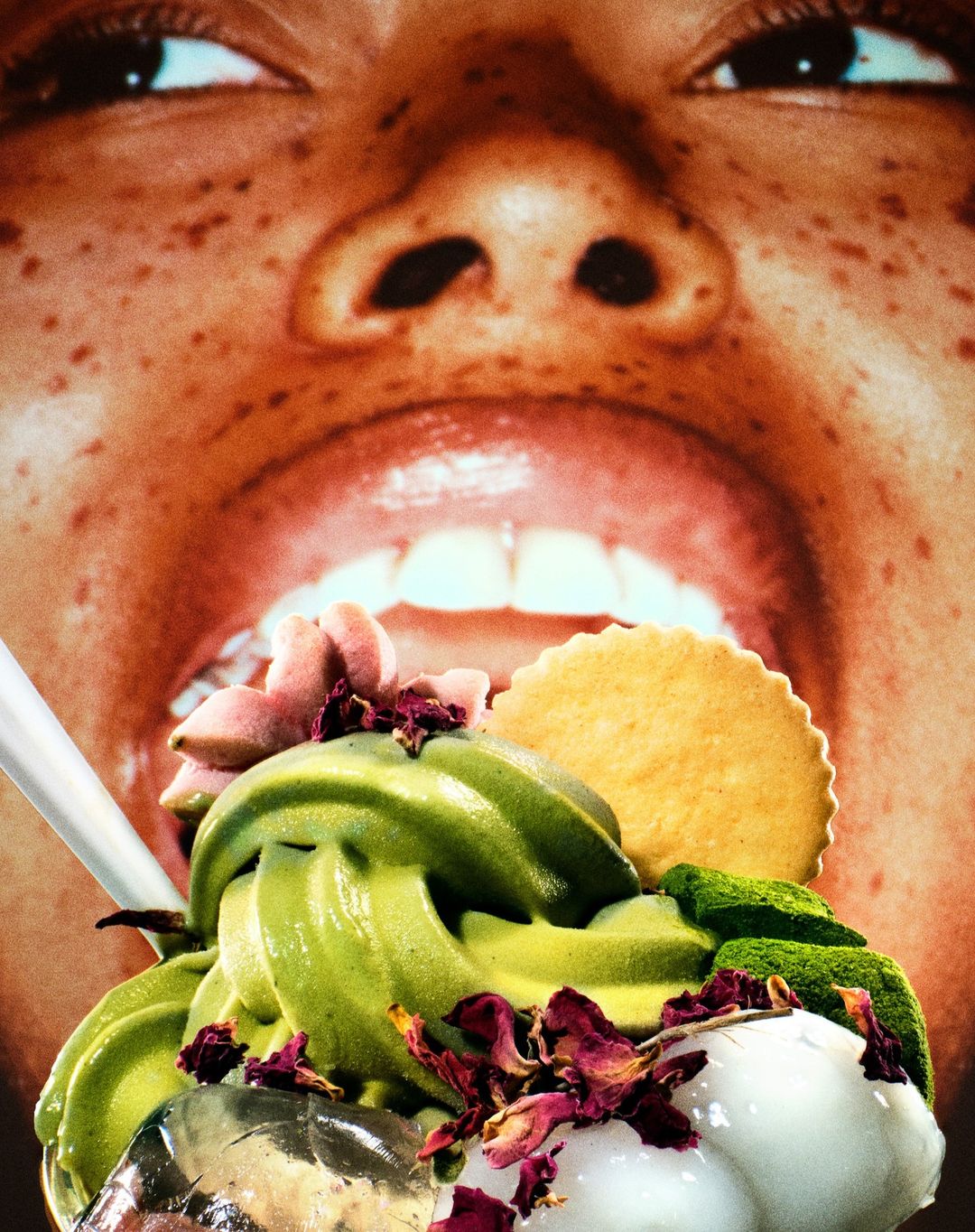 Close-up of matcha soft serve ice cream with toppings in front of person's face with mouth open, creating a surreal food portrait.