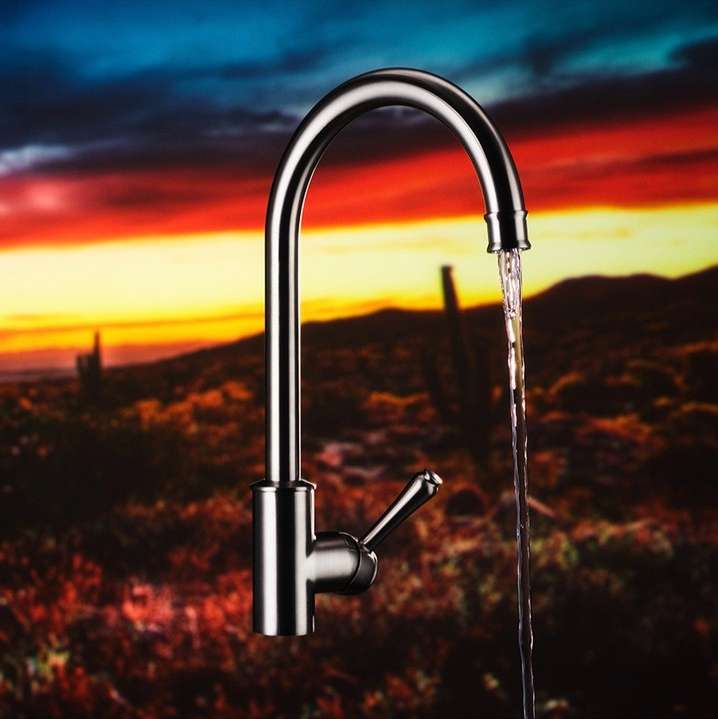 Stainless steel faucet dispensing water with a blurred desert landscape background featuring sunset colors and cacti.