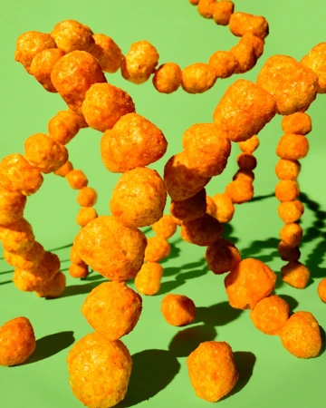 Close-up studio shot of cheese puff snack arranged in a DNA strand formation against a light green background with studio lighting.