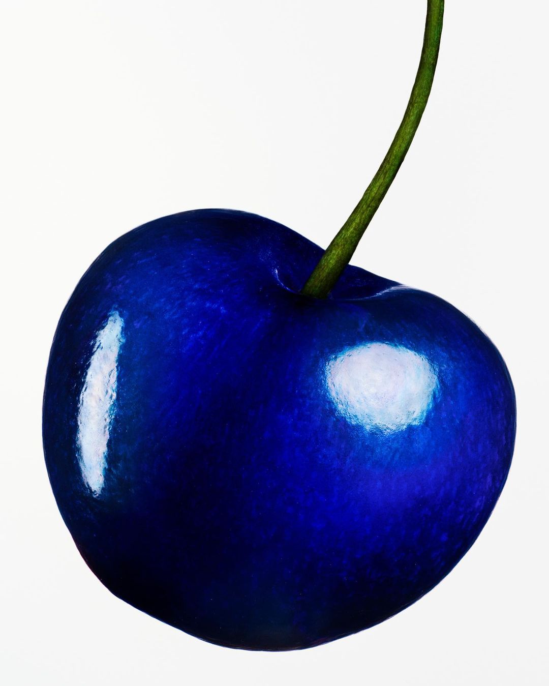 Close-up macro image of a single vibrant blue cherry with a green stem against a plain white background.
